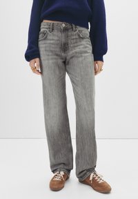 Jean en denim gris à coupe ample ; design cinq poches ; légère décoloration ; associé à des chaussures marron à lacets ; modèle portant un pull marine.