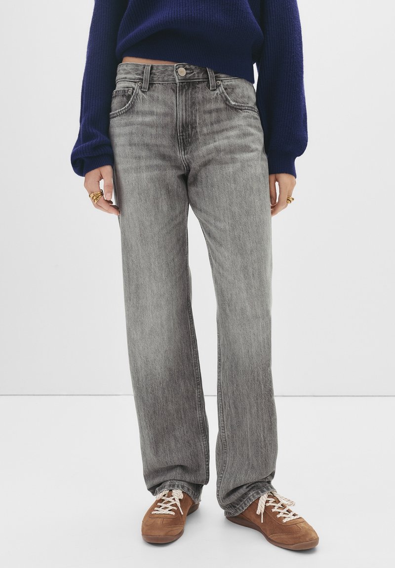 Jean en denim gris à coupe ample ; design cinq poches ; légère décoloration ; associé à des chaussures marron à lacets ; modèle portant un pull marine.