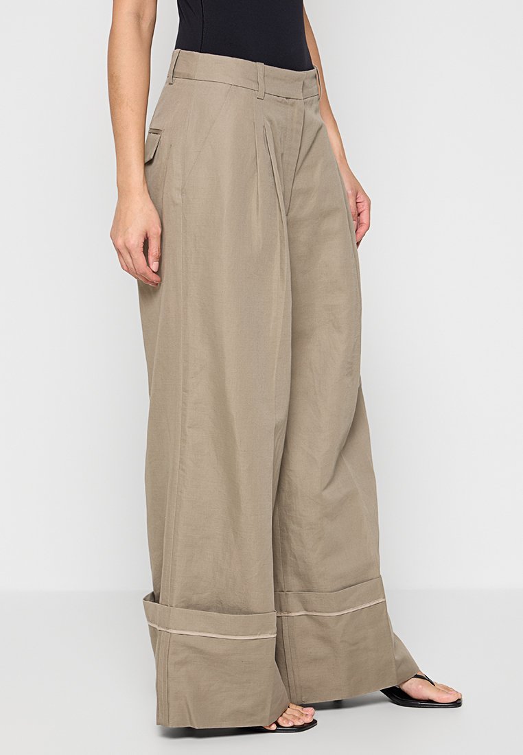 Beige wijde broek met een hoge taille, voorzien van voorplooien en zijzakken, gemaakt van een lichtgewicht stof met een zachte textuur.