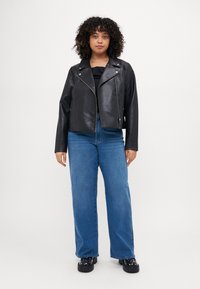 Black faux leather biker jacket with zip closure, angled lapels; paired with blue wide-leg jeans and black platform shoes.
