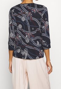 Camicetta navy con un design fluido presenta motivi paisley e geometrici in bianco, rosso e blu; maniche a tre quarti e vestibilità ampia.