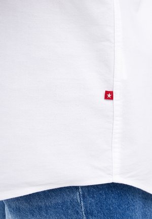 Biały materiał z czerwonym tagiem z białą gwiazdą w pobliżu szwu, w połączeniu z niebieskimi dżinsami z denimu.