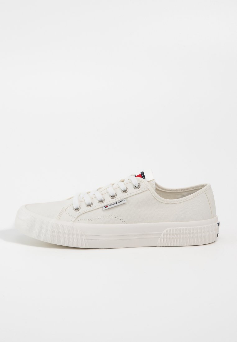 Zapatillas de lona en color crema con un acabado texturizado, que presentan una puntera redondeada, cordones blancos y un pequeño parche de logo en el lateral.