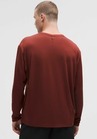 Mörkröd långärmad skjorta med rund halsringning och en ögla bak; slät textur och avslappnad passform.