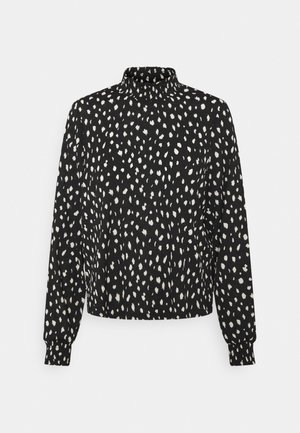 Blusa nera con pattern a pois bianchi, collo alto e maniche lunghe con polsini aderenti. Tessuto strutturato con vestibilità comoda.