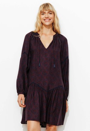 Robe noire à motifs avec un décolleté en V, des manches longues et une jupe froncée. Le tissu présente un motif géométrique subtil dans des tons de rouge et de bleu.