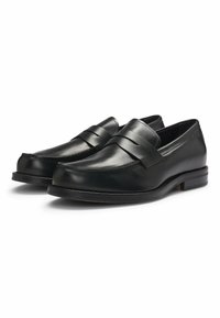 Black leather loafers with a smooth finish, featuring a decorative strap across the front, rounded toe, and a low-profile sole.