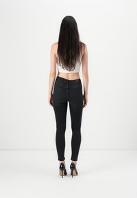 Zwarte skinny jeans met een aansluitend ontwerp, voorzien van achterzakken en een hoge taille. Gemaakt in combinatie met een witte cropped top en zwarte hoge hakken.