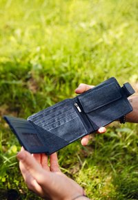 Dark blue fabric wallet with multiple card slots, zippered compartment, and a snap closure, held in a hand against a grassy background.