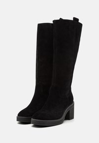 Botas de ante negras hasta la rodilla con tacón cuadrado, punta redondeada y un detalle de costura mínima a lo largo de las costuras. Material texturizado con un acabado suave.