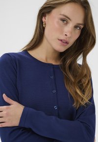 Marineblauer Strickcardigan mit Rundhalsausschnitt, langen Ärmeln und Knopfleiste vorne. Glatte Textur mit minimalen Details.