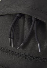 Tissu de sac à dos noir à surface texturée, doté de deux cordons noirs et d'une poche zippée au fond.