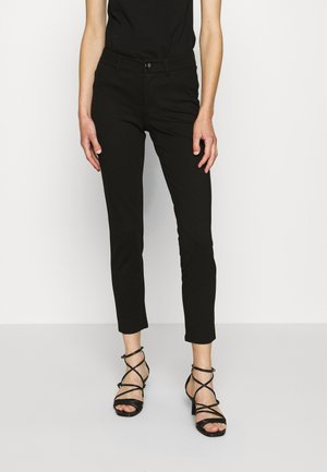 Černé zkrácené kalhoty s úzkým střihem, vybavené zapínáním na knoflíky a hladkou texturou, doplněné o černé sandály na podpatku s pásky.