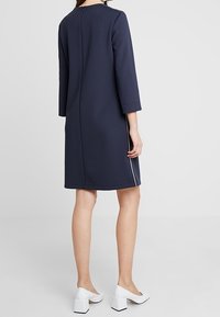 Abito navy con taglio dritto, maniche a tre quarti, zip sul retro e rifiniture bianche ai lati. Indossato con scarpe bianche con tacco block.