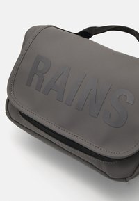Grå vanntett bag med teksturert overflate, med det fete ordet "RAINS" foran, glidelåslukking, og et svart stoffhåndtak.