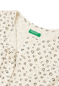 Blusa crema con un patrón de leopardo, que presenta un cierre de botones en el frente y una textura suave. La etiqueta dice "United Colors of Benetton".