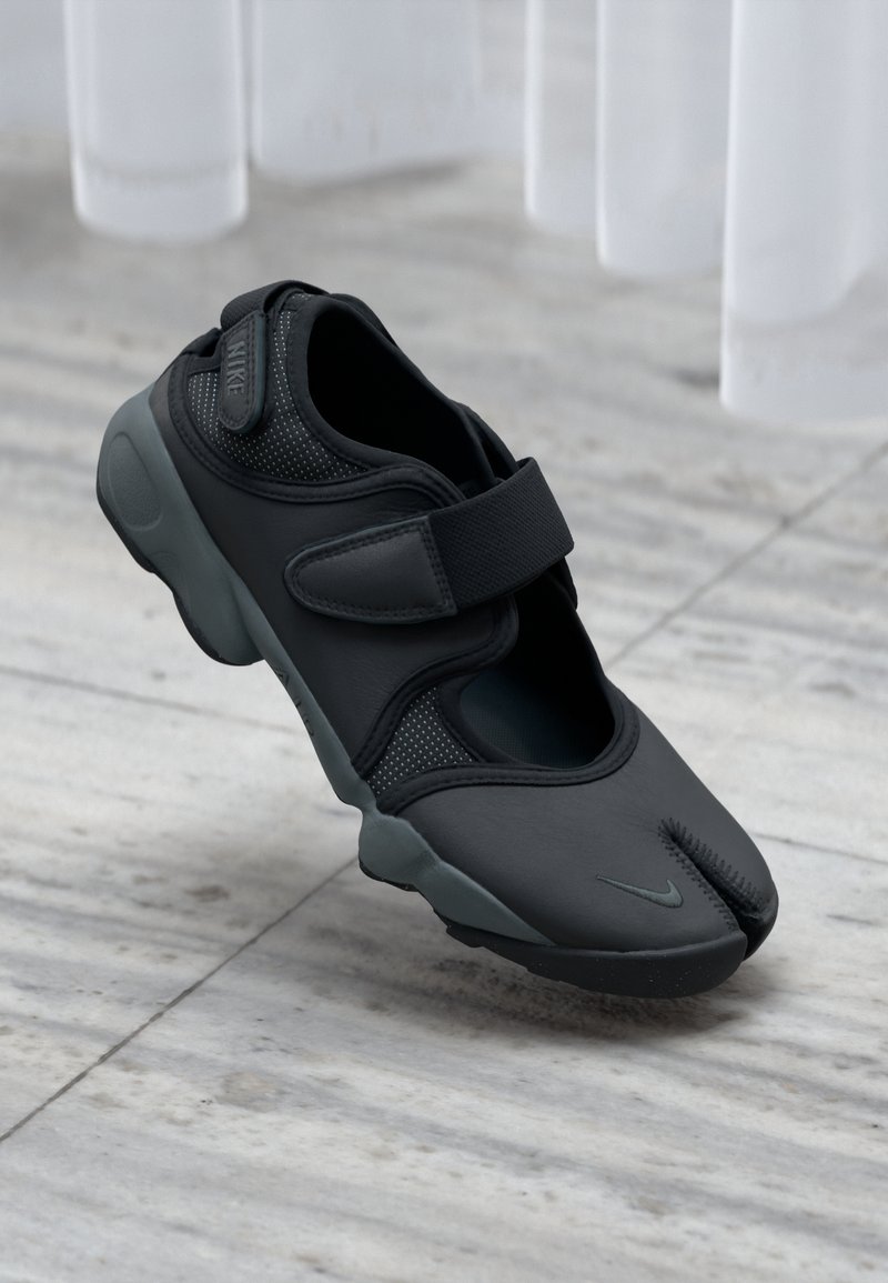 Nike črne športne čevlje z razdeljenim prstom, z zračnimi mrežastimi detajli in varnim trakom, ki imajo mehko, teksturirano zgornje material.