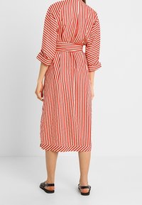 Rød- og hvidstribet kjole med trekvartlange ærmer, taljebånd og knælængde, lavet af letvægtstof med afslappet pasform.