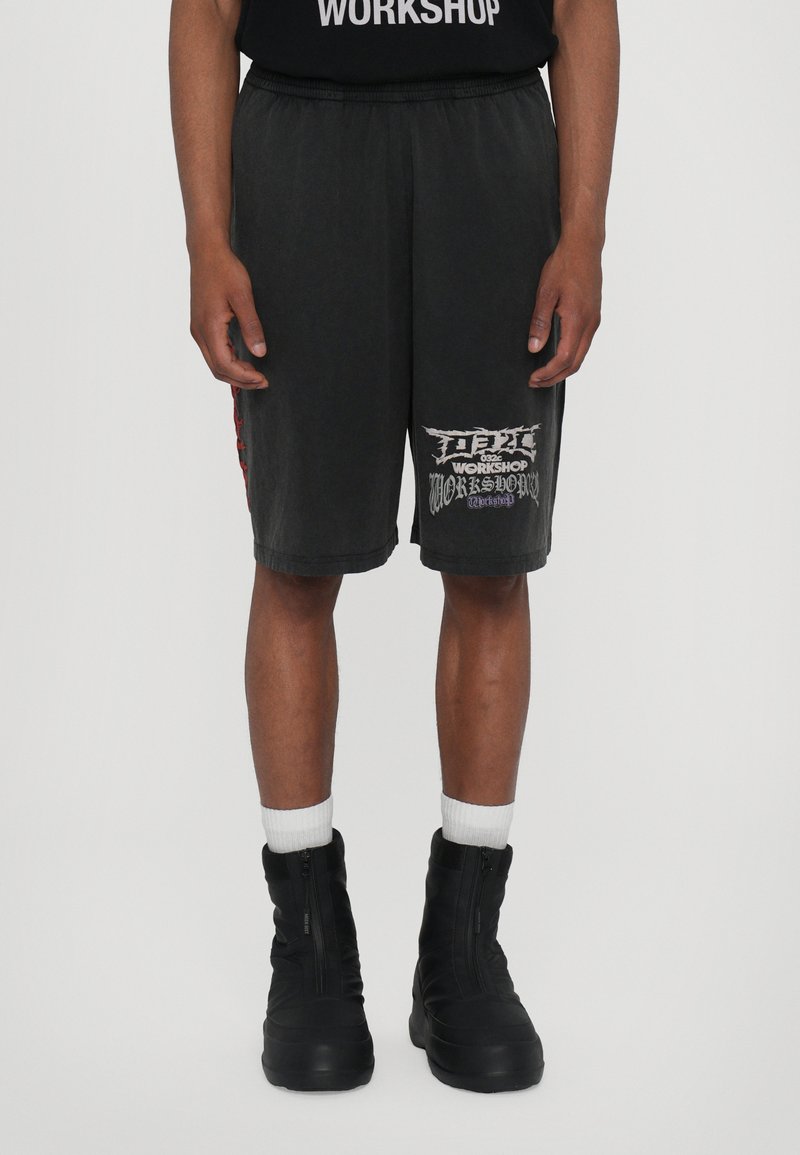 Pantalones cortos negros de corte relajado, con un estampado lateral y detalles en rojo, hechos de una suave mezcla de algodón, combinados con botas altas negras con cremallera.