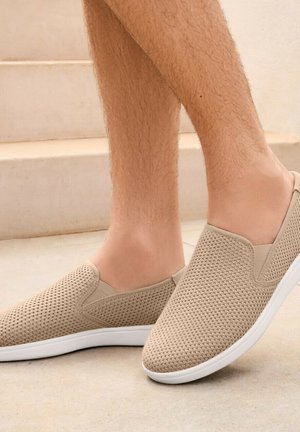 Beige instap schoenen met een textuur van gaas en een witte rubberen zool. Lichtgewicht ontwerp. Geschikt voor casual gebruik en gemakkelijk aan te trekken.