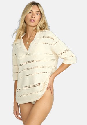 Maglione di colore crema, lavorato a maglia larga, con maniche corte, caratterizzato da strisce a trama aperta e scollo a V. Silhouette casual con spacchi laterali.