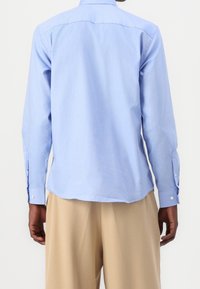 Vaaleansininen, pitkähihainen nappipaitapaita, pehmeä materiaali, suora leikku, klassinen kaulus. Hihansuissa napilliset hihansuut ja takana yläosa onosta yksityiskohta.