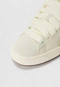 Nahaufnahme einer cremefarbenen Wildledersneaker-Spitze mit dicken, passenden Schnürsenkeln und einer strukturierten, schmutzig-weißen Gummisohle.