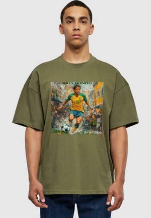 Oliven grøn oversized t-shirt med et trykt grafik af en fodboldspiller i en gul og blå uniform, med teksten "JOGA BONITO."