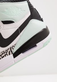 Černobílé kožené tenisky s akcenty máty, texturovanými panely a gumovou podrážkou s viditelnou vzduchovou odpružovací jednotkou.