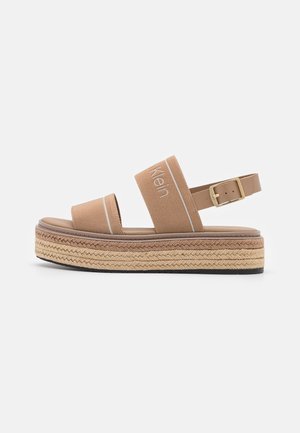 Sandale à plateforme beige avec deux brides en tissu, dont une brodée de texte, semelle en corde tressée et bride de cheville ajustable avec boucle.