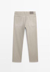 Pantalon beige à jambes droites avec deux poches arrière, passants pour ceinture et une petite étiquette rectangulaire sur la ceinture.