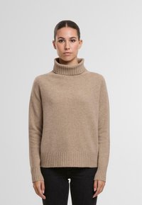 Beige Rollkragenpullover mit geripptem Kragen und Saum. Weiche Textur, lange Ärmel und lockere Passform, kombiniert mit schwarzen Jeans.
