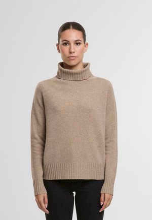 Beige Rollkragenpullover mit geripptem Kragen und Saum. Weiche Textur, lange Ärmel und lockere Passform, kombiniert mit schwarzen Jeans.