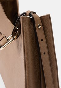 Brown leather handbag with a textured finish, featuring a gold-tone hardware accent and a detachable strap.