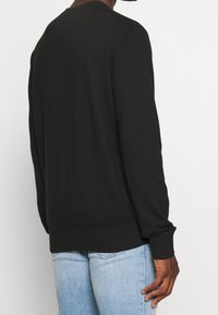 Schwarzer langärmliger Crewneck-Pullover aus weichem Stoff, mit gerippten Bündchen und Saum, einem lockeren Schnitt und minimalen Nähdetails.