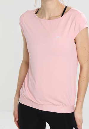 Femme portant un haut de sport à manches courtes rose clair et un soutien-gorge de sport noir, associé à un legging noir sur un fond uni.