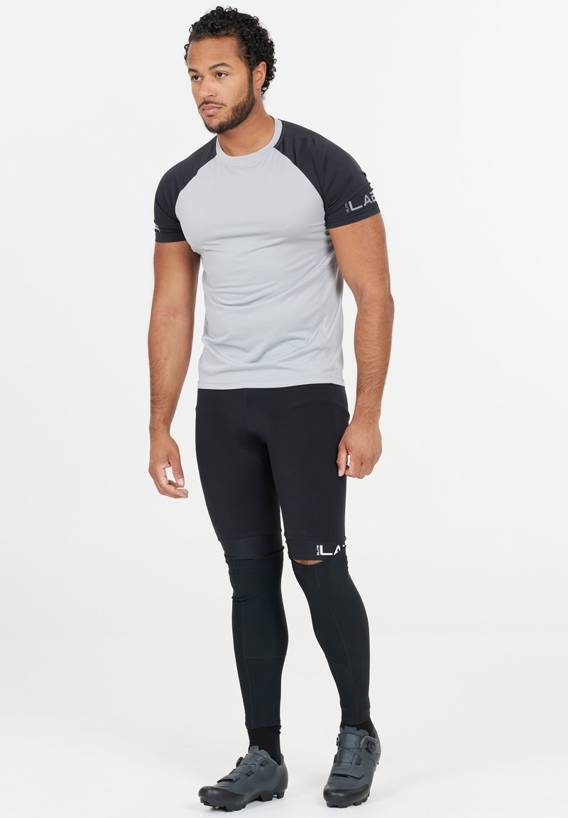 Kortärmad, ljusgrå träningsskjorta med svarta raglanärmar, kombinerad med svarta tajta leggings och grå cykelskor.