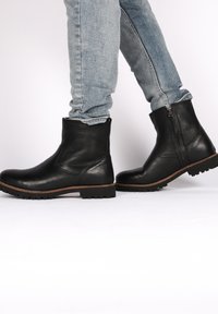 Stivali alla caviglia in pelle nera con finitura testurizzata, punta tonda, cerniere laterali e suole robuste, abbinati a jeans in denim blu chiaro.