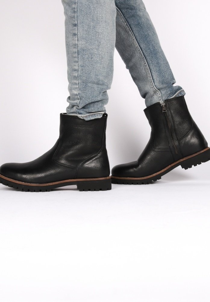 Stivali alla caviglia in pelle nera con finitura testurizzata, punta tonda, cerniere laterali e suole robuste, abbinati a jeans in denim blu chiaro.