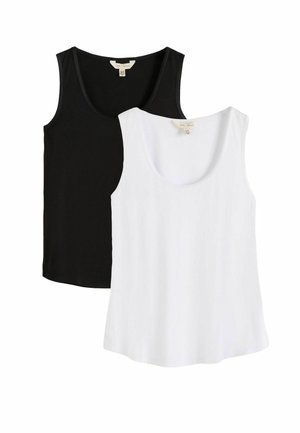 Sötét hajú nő fekete ujjatlan felsőben és világos színű nadrágban, egyik kezét a nyaka közelében tartva egy semleges háttér előtt pózol.