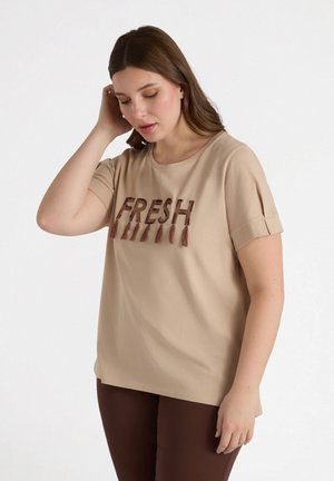 Camiseta de manga corta beige con el texto bordado "FRESH" en marrón, que presenta un cuello redondo y acentos de manga enrollada. Textura de tejido suave.