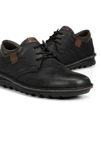 Zapatos de cuero negro con acabado liso, con detalles marrones, punta redondeada y suela texturizada para mayor agarre. Diseño clásico con cordones.