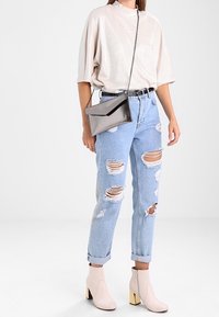 Vaaleanbeige ylisuuria yläosia, vaalensinisiä revittyjä farkkuja suurilla repeämillä, vaaleanpunaiset nilkkurit, joissa on paksut korot, ja kiiltävä harmaa clutch-laukku.