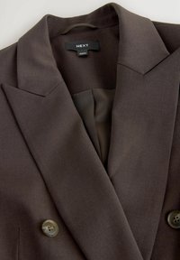 Bruine blazer van een gladde, gestructureerde stof. Voorzien van een scherpe revers, dubbele knoopsluiting en een zijden binnenvoering. Etiket: NEXT.