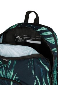 Reppu tummansinisestä kankaasta, jossa on vihreitä kasvimaisia kuvioita, vesitiivis pinta ja heijastava sisäosien yksityiskohtaus.