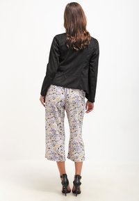 Černá bunda s přiléhavým střihem, kombinovaná s fialovými kalhotami s motivem vírů ve žlutých a tmavých tónech, nošená s černými podpatky.