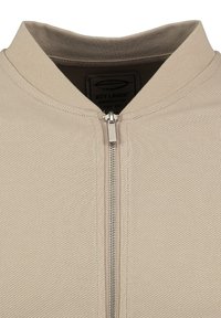 Chaqueta beige con cremallera y tejido texturizado, con cuello alzado y una cremallera de metal elegante. El forro interior es de un color contrastante.