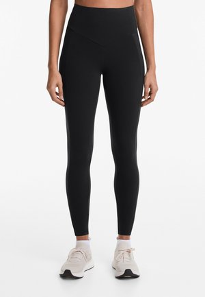Leggings neri a vita alta realizzati in un tessuto liscio e elastico con un design senza cuciture e pannelli laterali discreti. Accoppiati con scarpe da ginnastica leggere.
