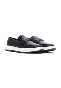 Zwarte leren instap schoenen met een gestructureerde bovenkant, een vlakke witte rubberen zool en een decoratieve band over de voet.