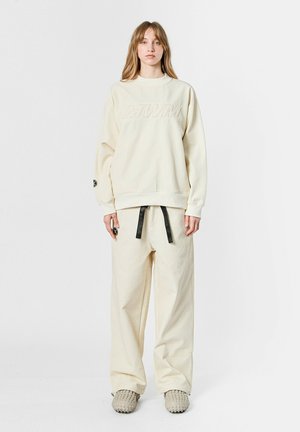 Sudadera texturizada color crema con el logo embossado "MWM", combinada con pantalones de pierna ancha a juego que cuentan con un cordón y parches de acento.